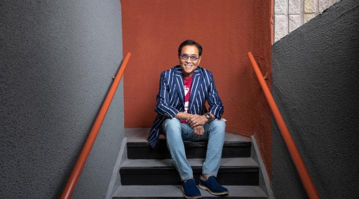Robert Kiyosaki sitting in the stairs smiling during a photo shoot. 