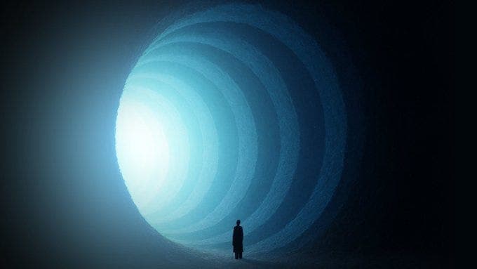 A silhouette of a person standing in front of a tunnel of light. The tunnel has concentric circular patterns that emit a bright blue light, creating a sense of depth and perspective. The person is facing towards the light, suggesting a journey or transition.